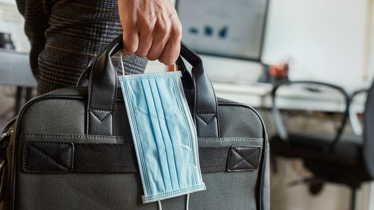 closeup of a young man in an office holding a briefcase and a surgical mask in his hand