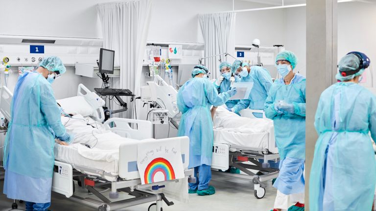 Medical professionals operating on patient in ICU. Doctors and nurses wearing protective coveralls. They are at hospital during pandemic.