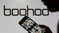 A woman poses with a smartphone showing the Boohoo app in front of the Boohoo logo on display in this illustration