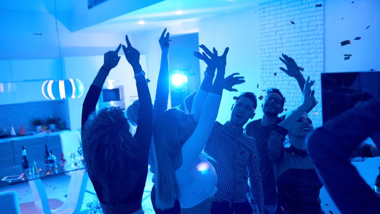 Group of modern young people dancing under confetti at private house party lit by blue light