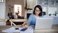 Shot of a young woman using a laptop and calculator while working from home