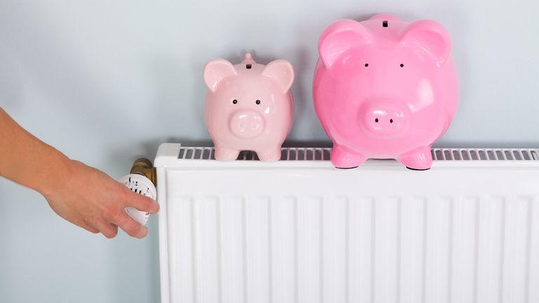 Person Hand Adjusting Thermostat With Two Piggy Banks On Radiator To Save Money At Home
ALAMY