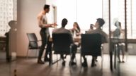 Business Presentation, Blurred Background. Businessman Giving Speech During Seminar With Coworkers In Office, Standing At Desk In Boardroom, Diverse People Sitting At Table And Listening To Speaker