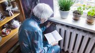 The senior woman holding gas bill in front of heating radiator. Payment for heating in winter.