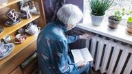 The senior woman holding gas bill in front of heating radiator. Payment for heating in winter.