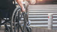 Disabled man on wheelchair preparing to cross the road on pedestrian crossing, copy space.