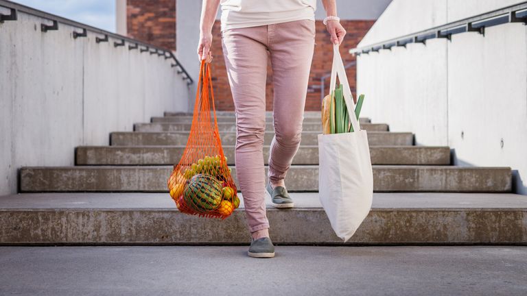 Woman walking at stairs and carrying reusable mesh bag after shopping groceries in city. Sustainable lifestyle with zero waste and plastic free