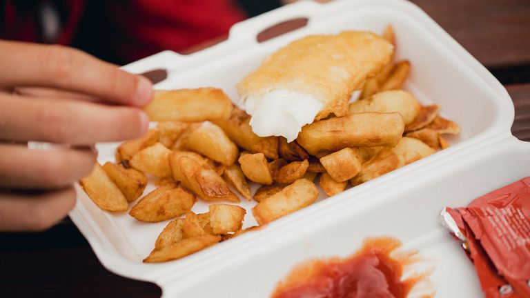 An unrecognisable person enjoying some fish and chips.