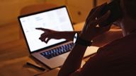 Unrecognizable man reading business report on a laptop computer and talking on a mobile phone while sitting at home office desk.