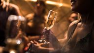 Close up of unrecognizable woman with glass of Champagne in a club. There are people in the background.