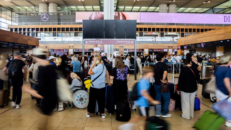 Numerous passengers wait in front of a black display board at the capital's Berlin Brandenburg Airport, in Schönefeld, Germany, Friday July 19, 2024. Air traffic has been suspended at BER Airport. A widespread Microsoft outage was disrupting flights, banks, media outlets and companies around the world on Friday. (Christoph Soeder/dpa via AP)