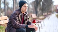 A man holds a rose alone on a bench. Pic: iStock